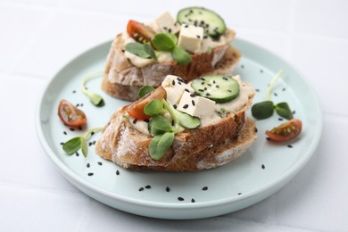 Photo of Tasty vegan sandwiches with tofu, cucumber, tomato and sesame seeds on white tiled table, closeup