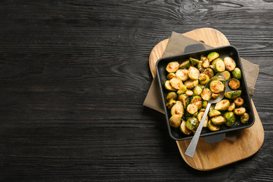 Photo of Delicious roasted brussels sprouts with grated cheese on black wooden table, top view. Space for text