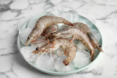Photo of Raw shrimps with ice on marble table