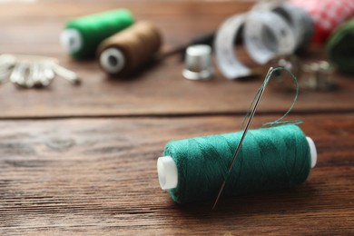 Photo of Green sewing thread with needle on wooden table. Space for text