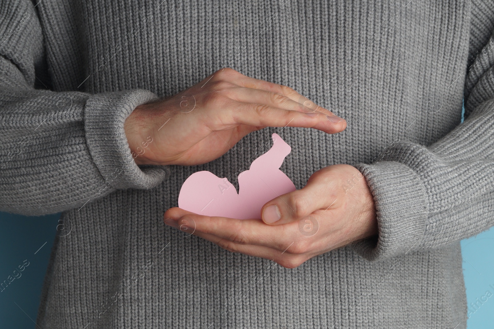 Photo of Female health. Man holding newborn paper figure on light blue background, closeup