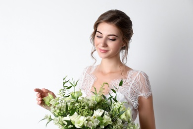 Photo of Young bride wearing wedding dress with beautiful bouquet on light background