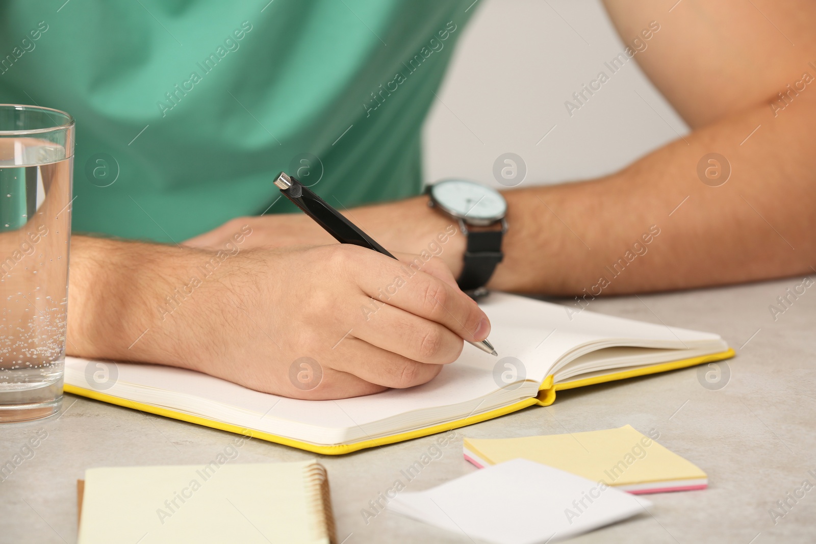 Photo of Man writing in notebook at table indoors, closeup