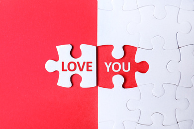 Image of White puzzle with separated piece and phrase LOVE YOU on red background, top view