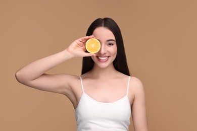 Beautiful young woman with piece of orange on beige background