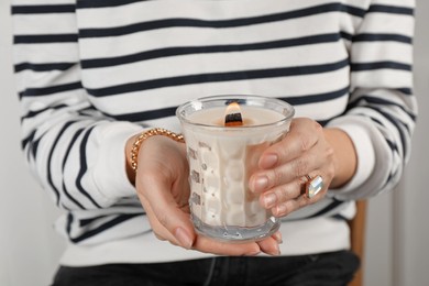 Photo of Woman with stylish jewelry holding burning soy candle on light background, closeup