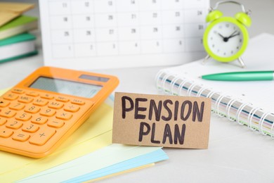 Photo of Card with words Pension Plan, calculator and stationery on white office table, closeup