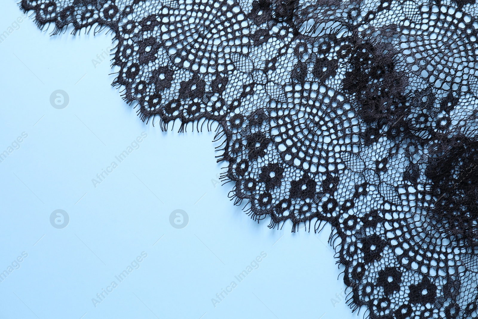 Photo of Black lace on light blue background, top view. Space for text