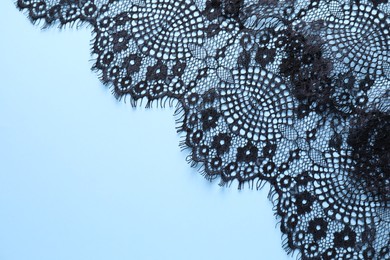 Black lace on light blue background, top view. Space for text