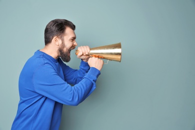 Photo of Young man shouting into megaphone on color background