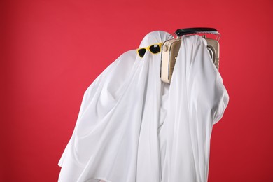 Photo of Person in ghost costume and sunglasses using retro radio receiver on red background