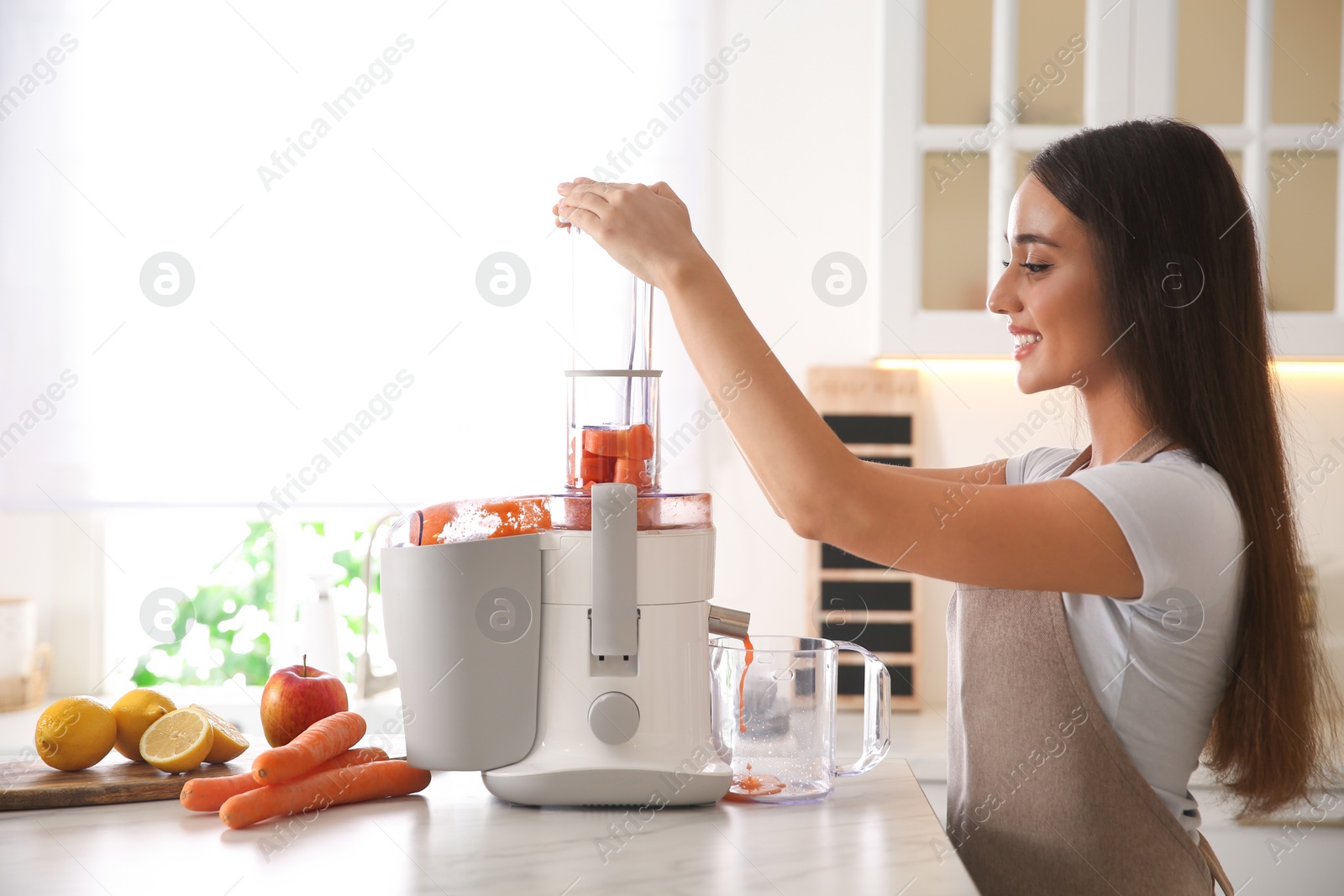 Photo of Young woman making tasty fresh juice at table in kitchen