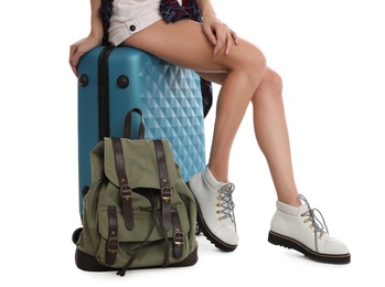 Photo of Woman sitting on suitcase near backpack against white background, closeup. Summer travel