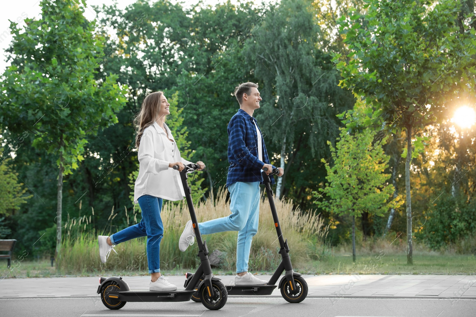 Photo of Happy couple riding modern electric kick scooters in park