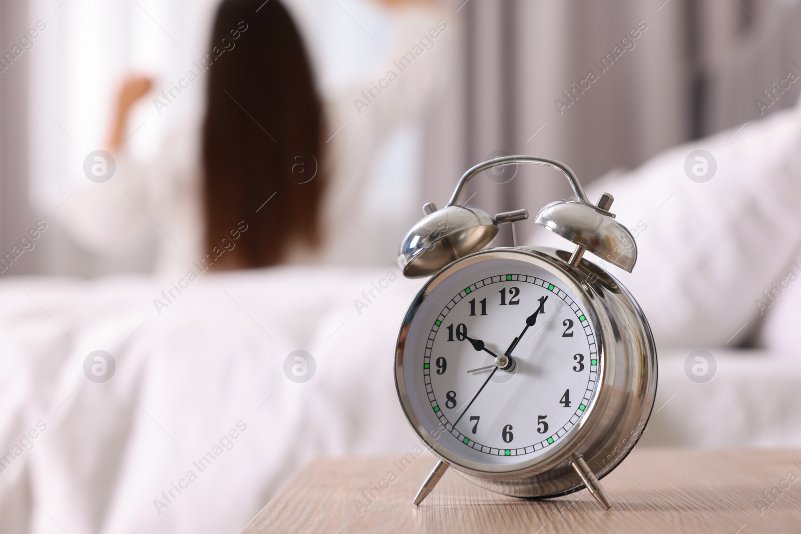 Photo of Alarm clock on nightstand. Woman awakening in bedroom, selective focus