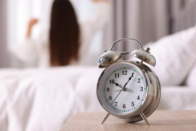 Photo of Alarm clock on nightstand. Woman awakening in bedroom, selective focus