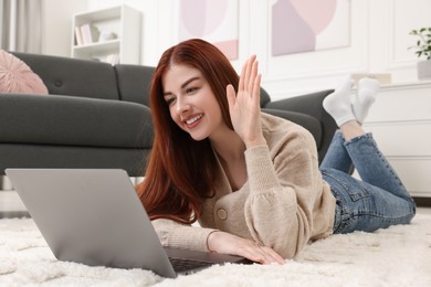 Happy woman with laptop having video chat on rug in living room