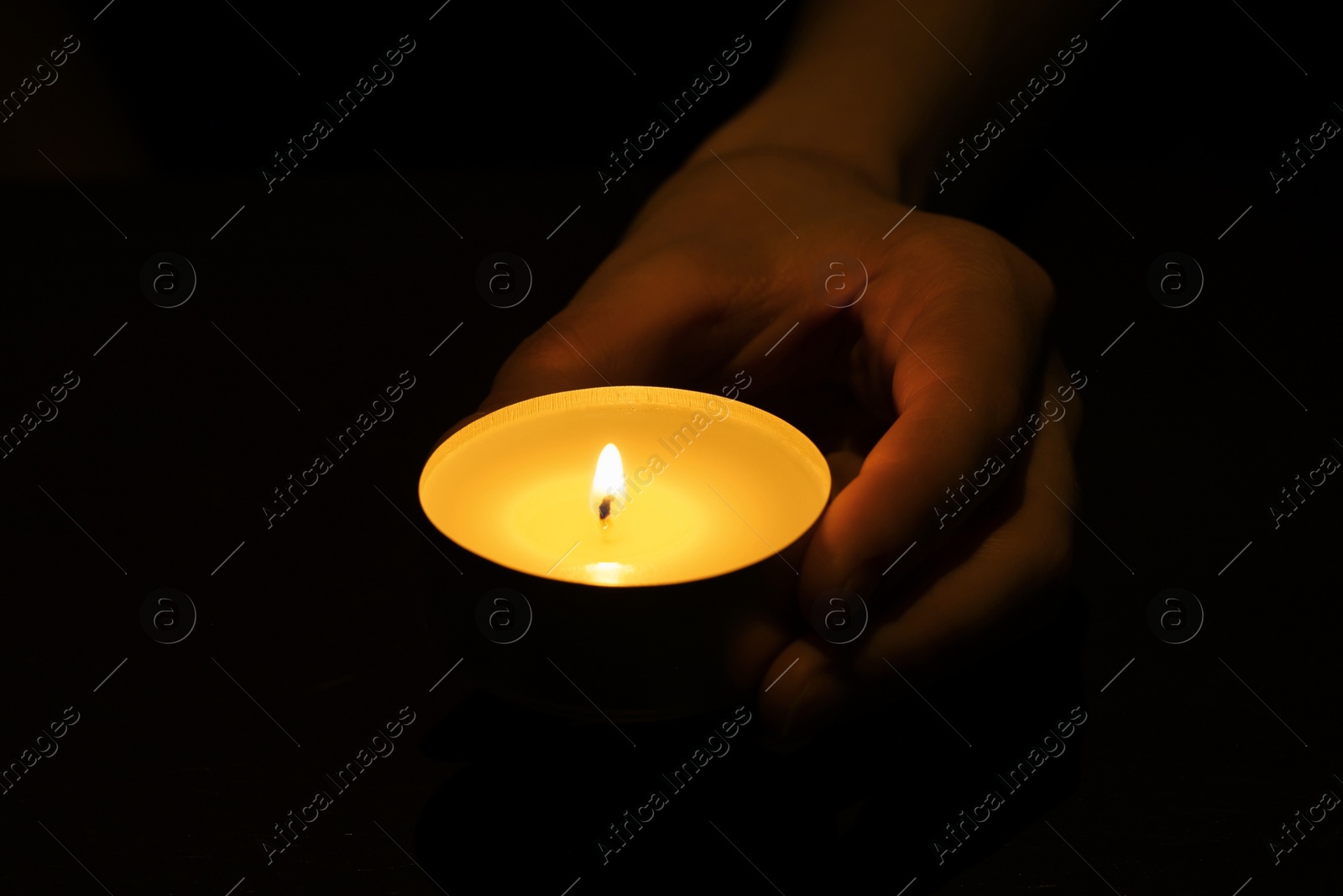 Photo of Woman holding burning candle in hand on black background, closeup