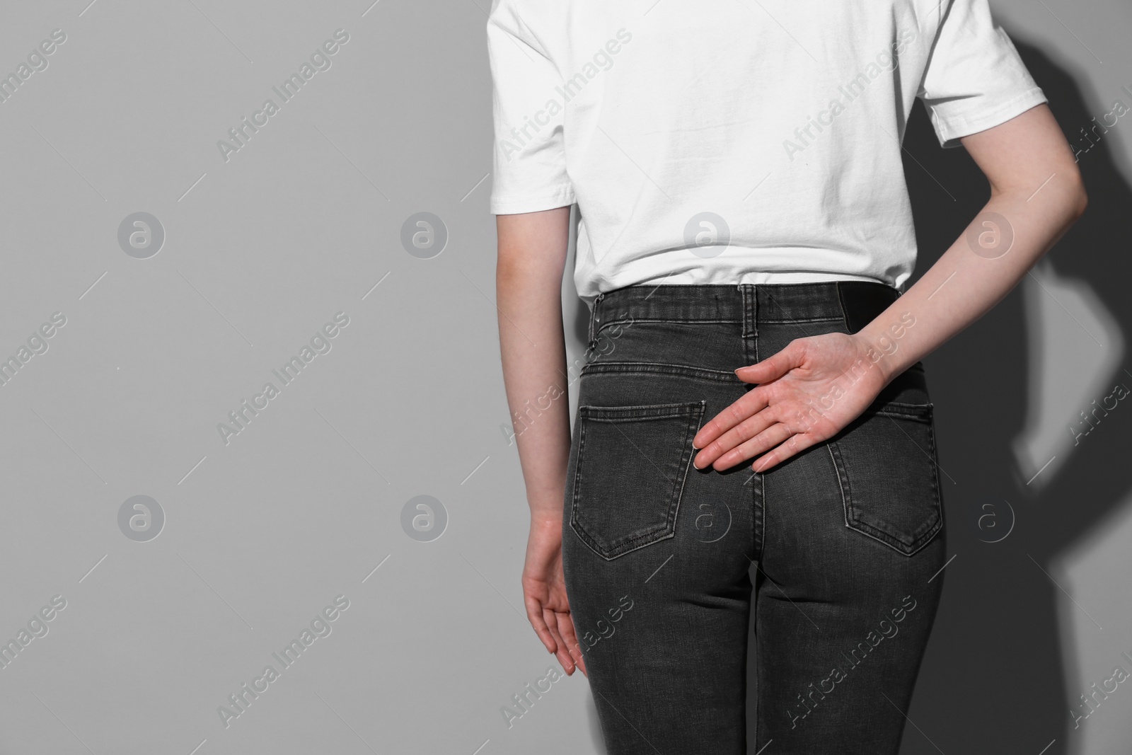 Photo of Woman showing open palm behind her back on grey background, back view. Space for text