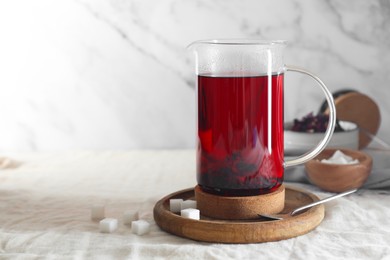 Photo of Delicious hibiscus tea in teapot and sugar cubes on table. Space for text