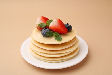 Photo of Stack of tasty pancakes with fresh berries and mint on beige background