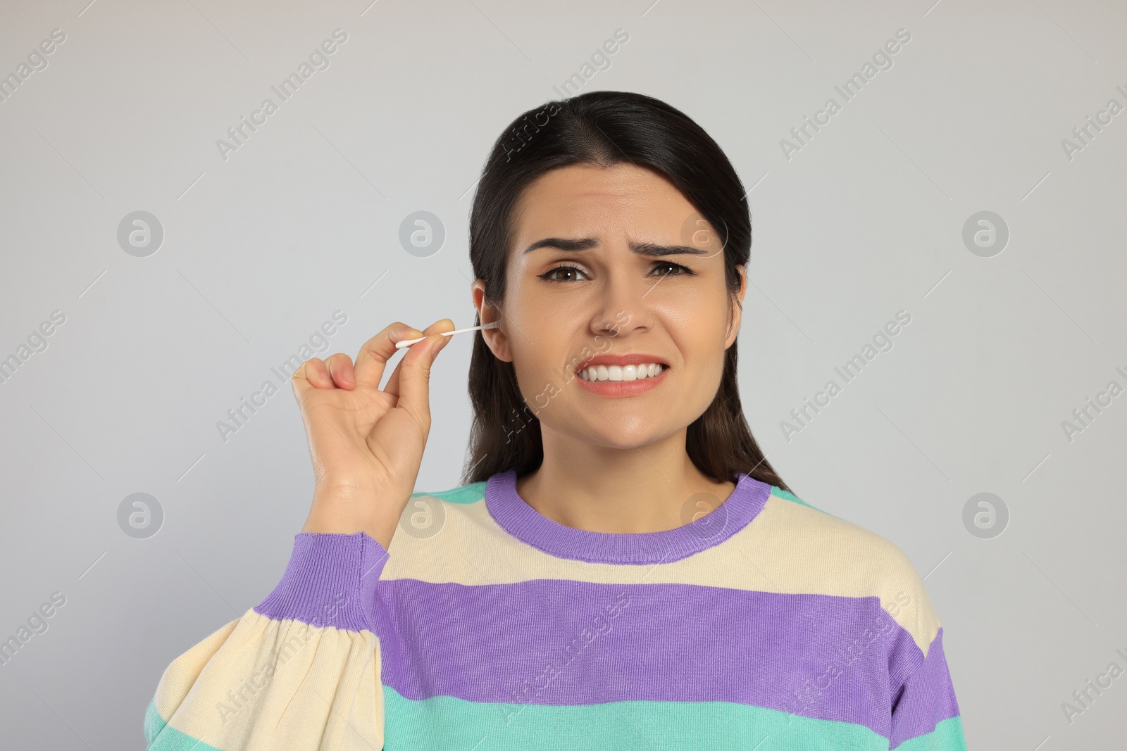 Photo of Young woman cleaning ear with cotton swab on light grey background