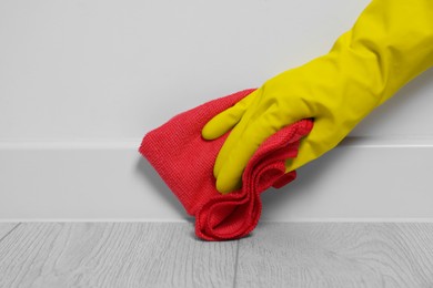 Photo of Woman in gloves cleaning plinth with cloth indoors, closeup