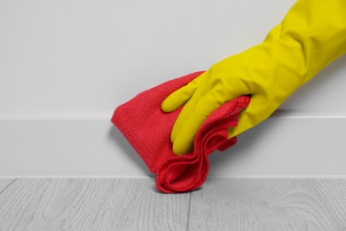 Woman in gloves cleaning plinth with cloth indoors, closeup