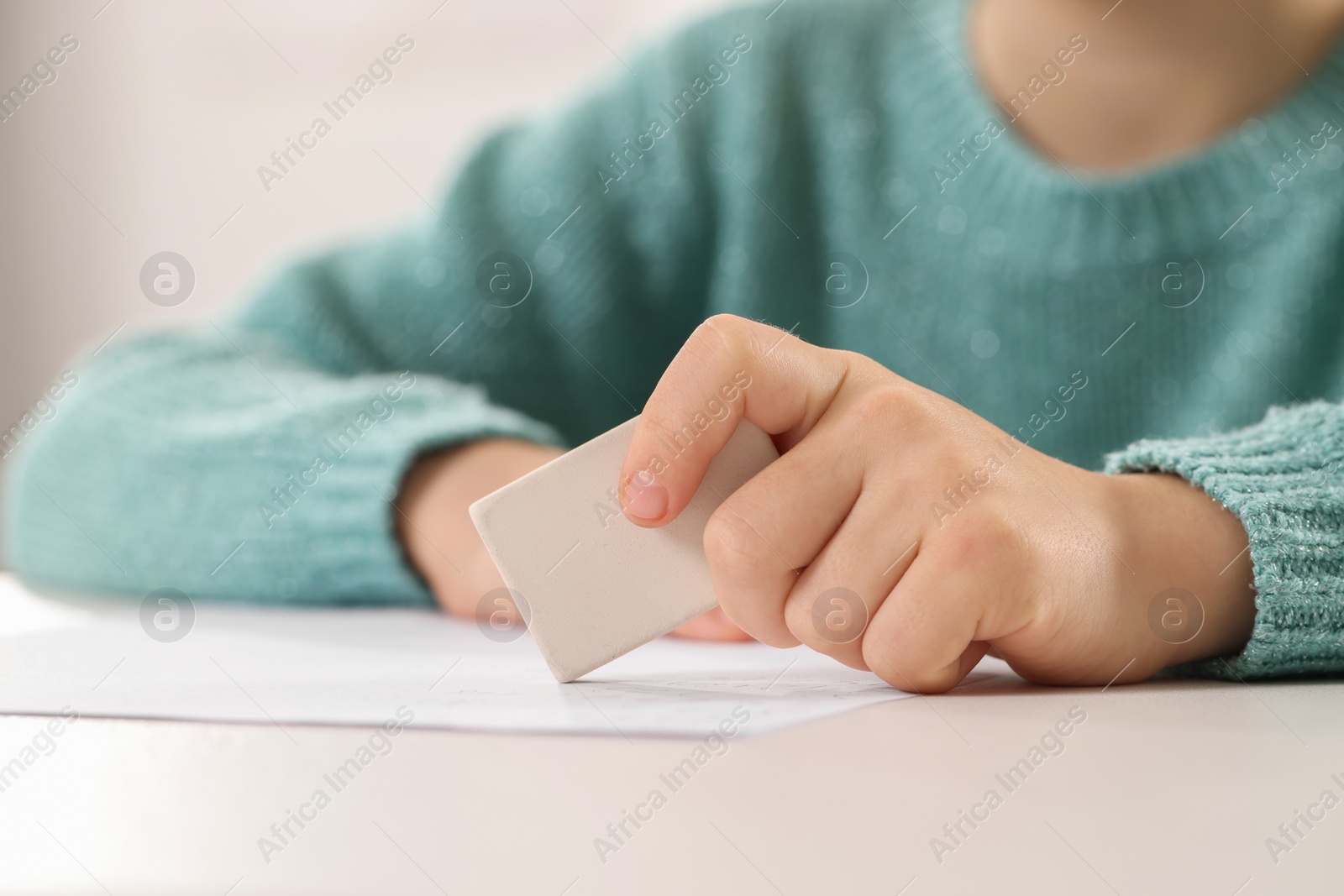 Photo of Girl erasing mistake in her homework at white desk, closeup