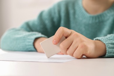 Photo of Girl erasing mistake in her homework at white desk, closeup