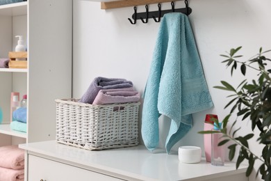 Photo of Fresh towels, laundry basket and toiletries on chest of drawers indoors