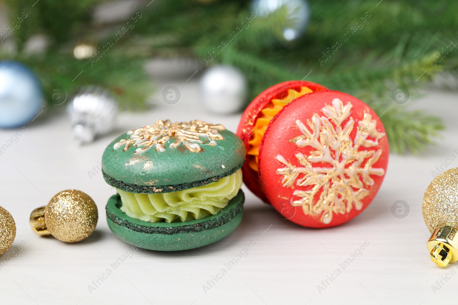 Photo of Different decorated Christmas macarons and festive decor on white wooden table, closeup