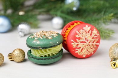 Different decorated Christmas macarons and festive decor on white wooden table, closeup