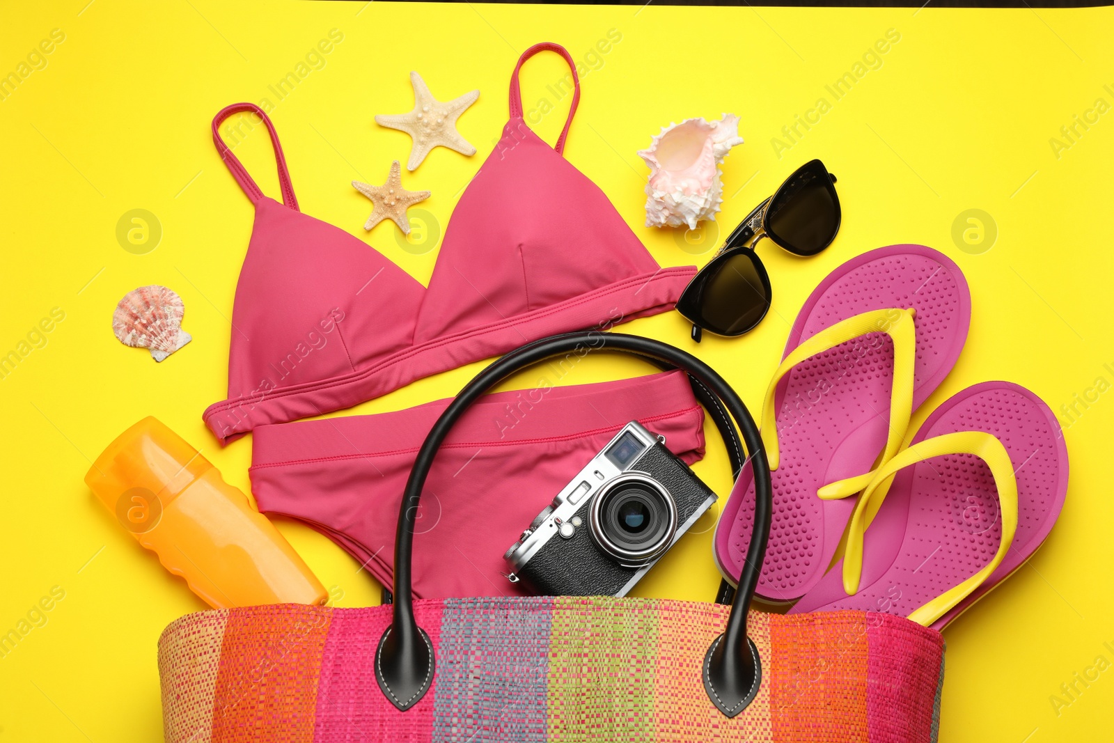 Photo of Stylish bag with beach accessories on yellow background, flat lay