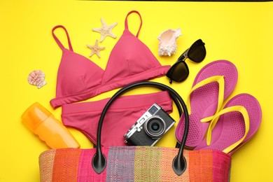 Photo of Stylish bag with beach accessories on yellow background, flat lay