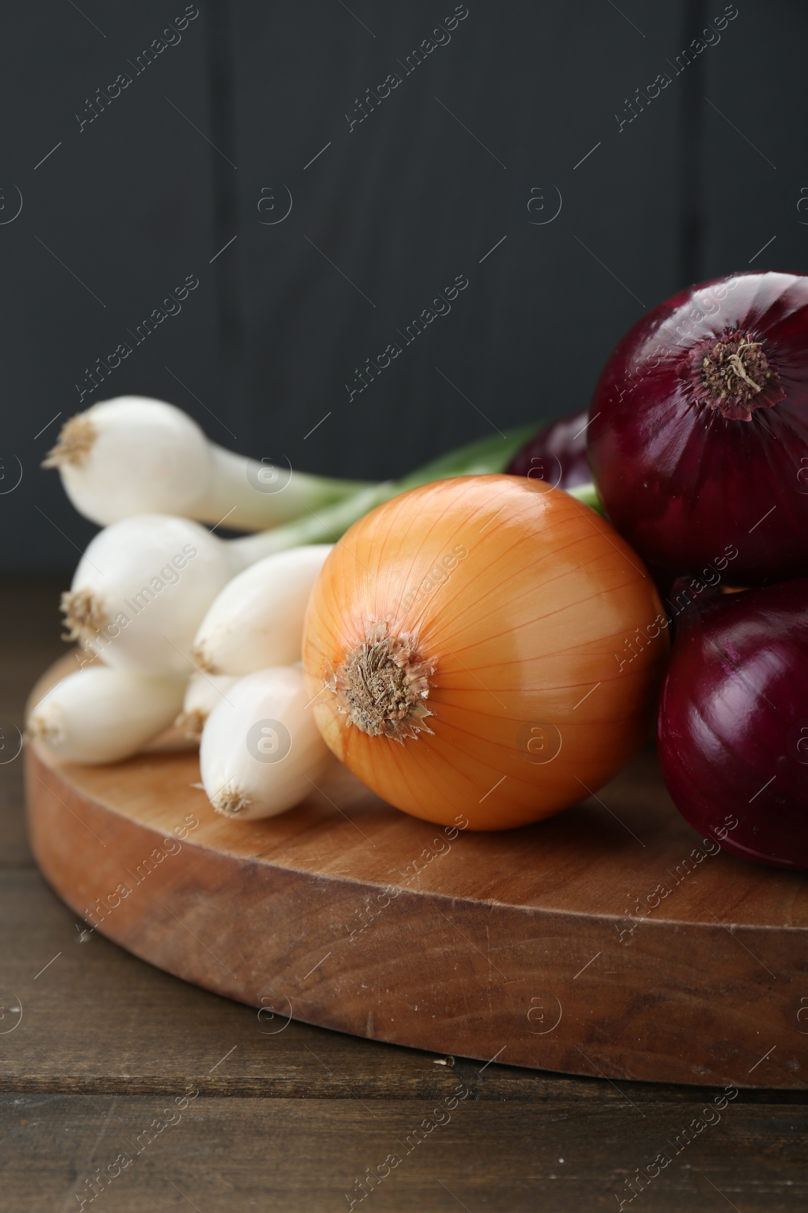 Photo of Board with different kinds of onions on wooden table, closeup