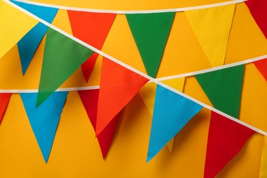 Photo of Buntings with colorful triangular flags hanging on orange background. Festive decor