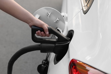 Photo of Woman inserting plug into electric car socket at charging station, closeup