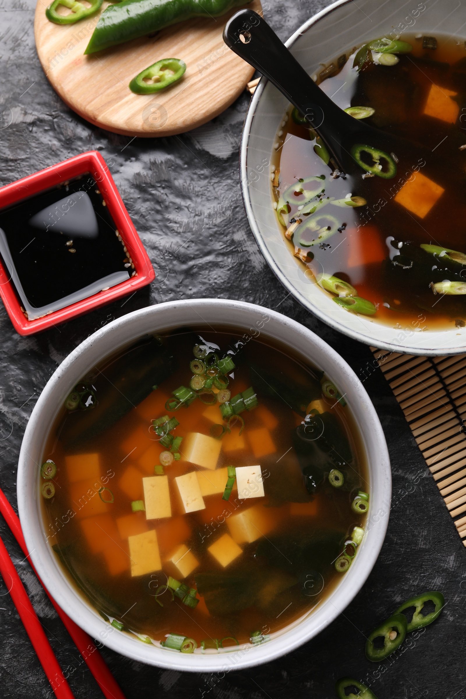 Photo of Delicious miso soup with tofu served on black textured table, flat lay
