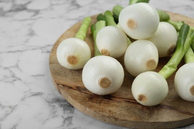 Photo of Wooden board with green spring onions on white marble table, closeup. Space for text