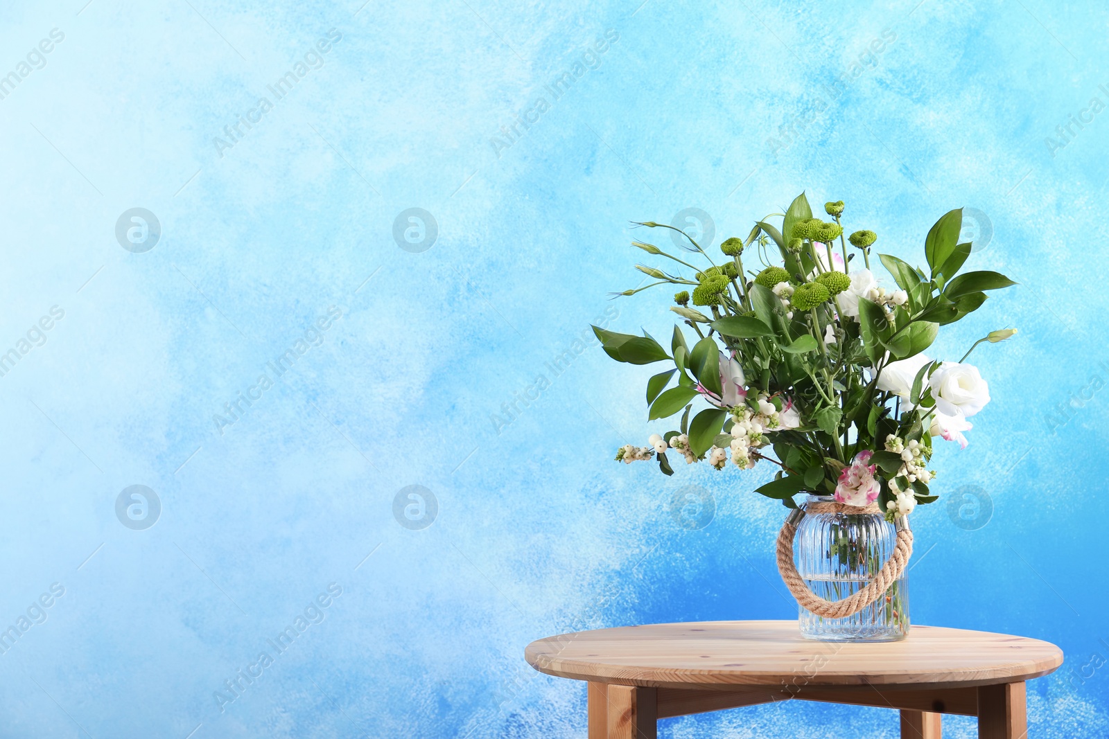 Photo of Vase with bouquet of beautiful flowers on table against color background. Space for text