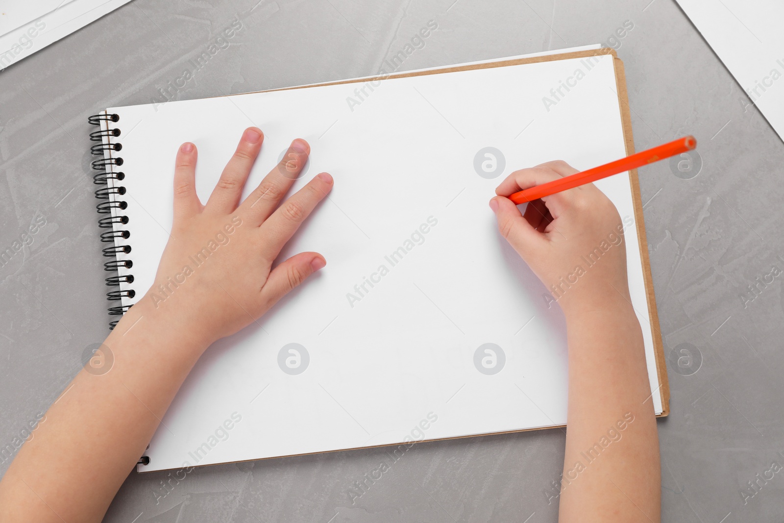 Photo of Little boy drawing with pencil at grey textured table, top view. Child`s art