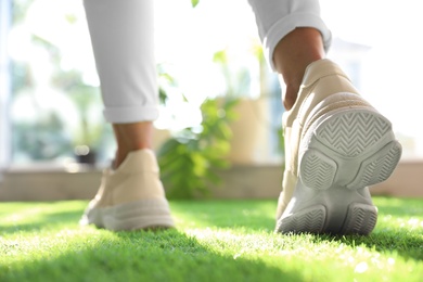 Photo of Young woman wearing stylish sneakers on green grass, closeup