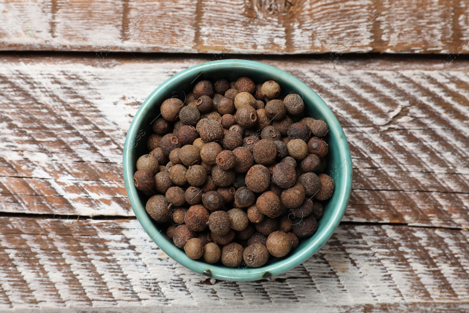 Photo of Aromatic allspice pepper grains in bowl on wooden table, top view