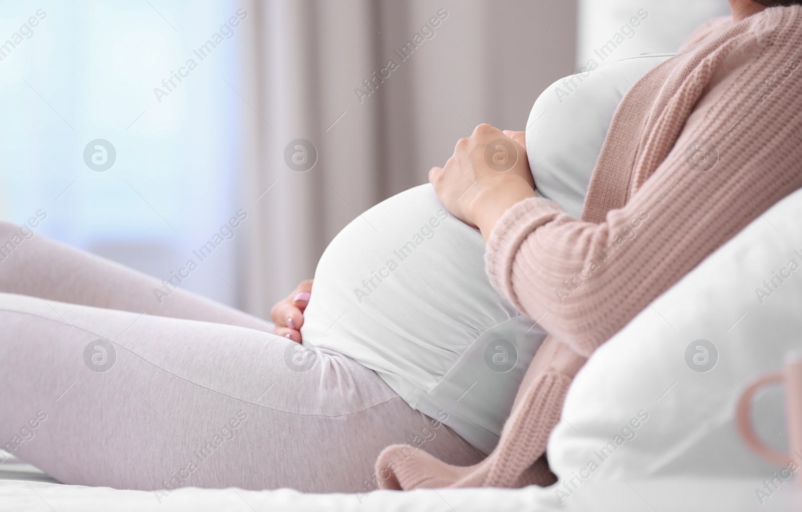 Photo of Young pregnant woman lying on bed and touching her belly at home, closeup