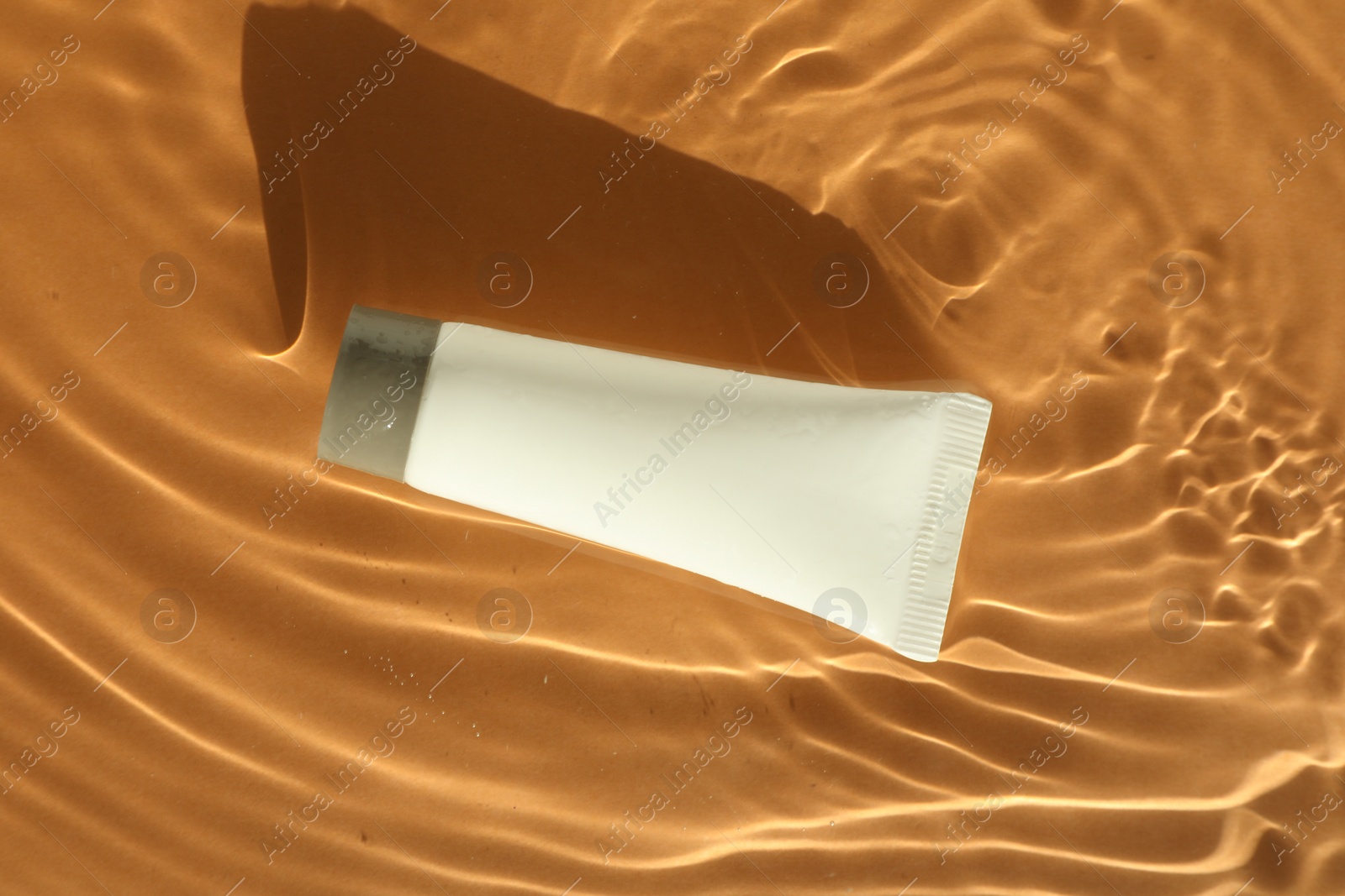 Photo of Tube with moisturizing cream in water on orange background, top view