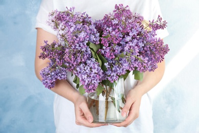 Young woman holding vase with beautiful blossoming lilac on color background. Spring flowers