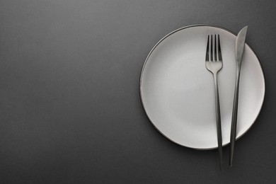 Clean plate, fork and knife on grey table, top view. Space for text
