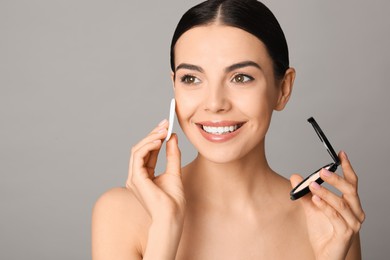 Photo of Beautiful young woman applying face powder with puff applicator on grey background