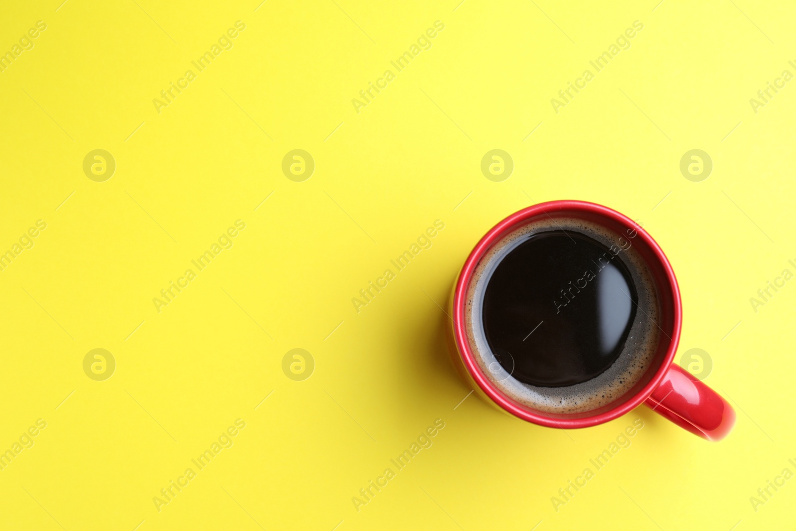 Photo of Fresh aromatic coffee in red mug on yellow background, top view. Space for text